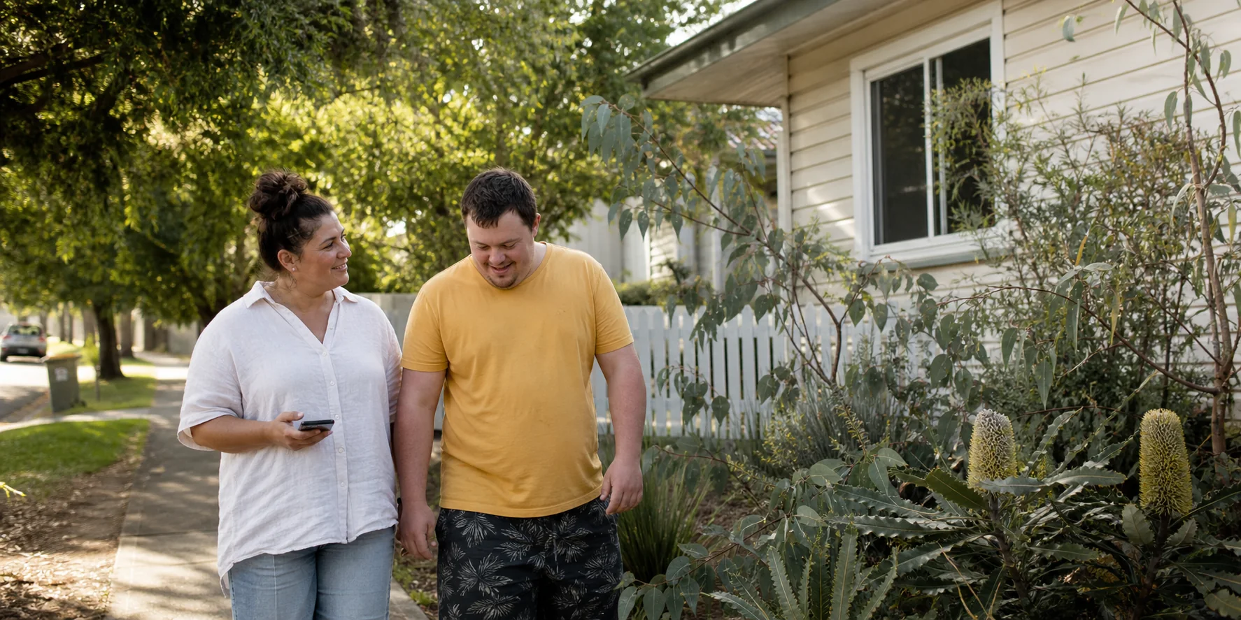 An adult participant and support worker walking together outside a Brisbane home